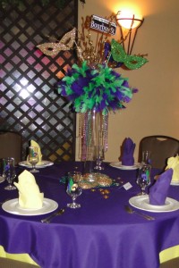 DIY Mardi Gras Centerpiece with tall glass cylinder, purple and green feathers, styrofoam masks, and Bourban St. sign