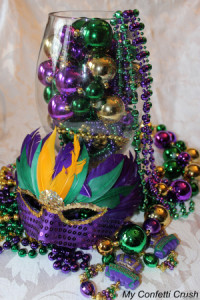 DIY Mardi Gras centerpiece with glass vase filled with beads and a feather mask leaned against it.