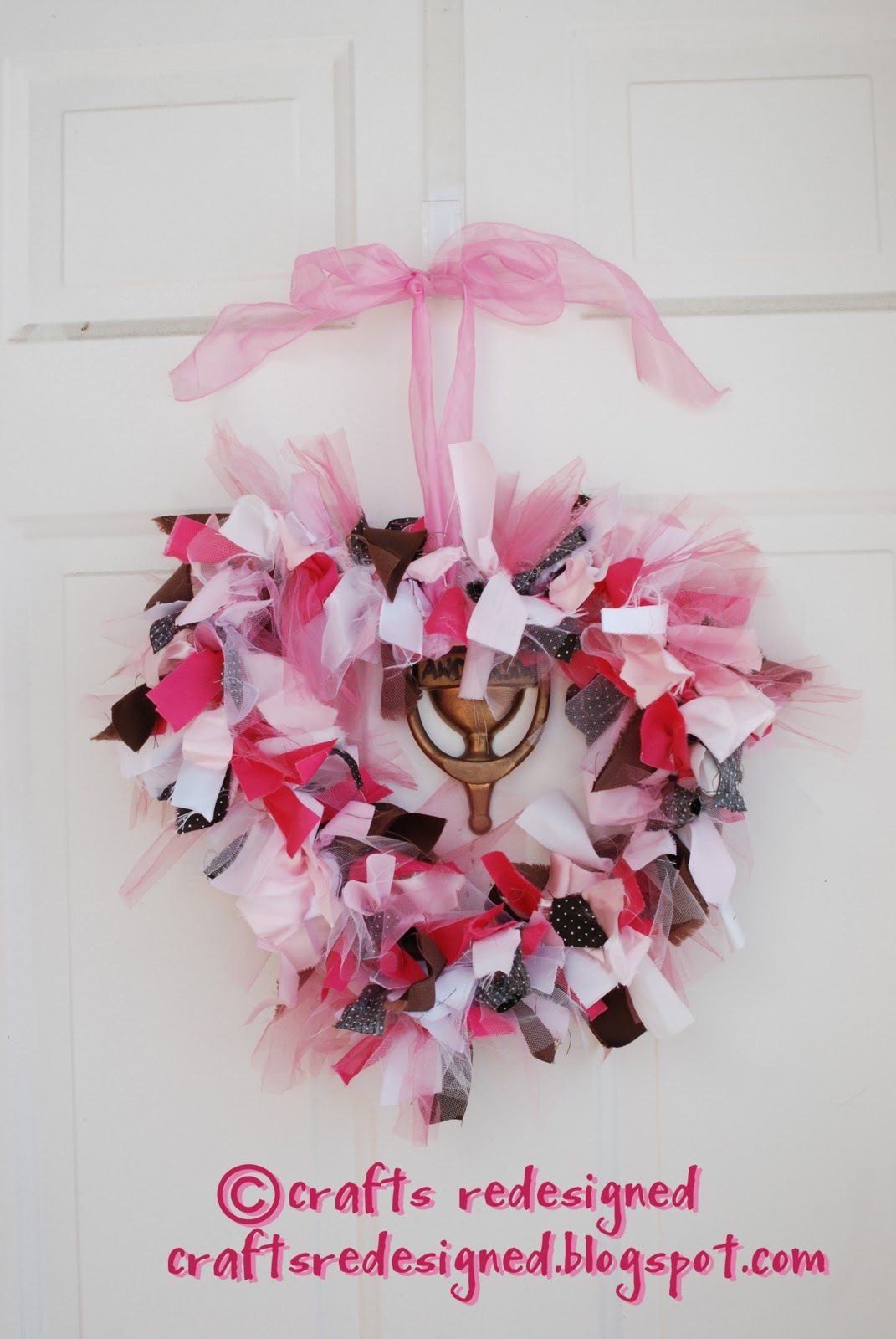Easy DIY Valentine's Door Wreath shaped like a heart with different shades of pink and a little bit of brown. Made with strips of fabric tied in a knot to a clothes hanger, and hanging from a large pink ribbon tied like a bow