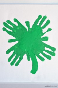 Four little green hand prints are used to create a piece of St. Patrick's Day art.